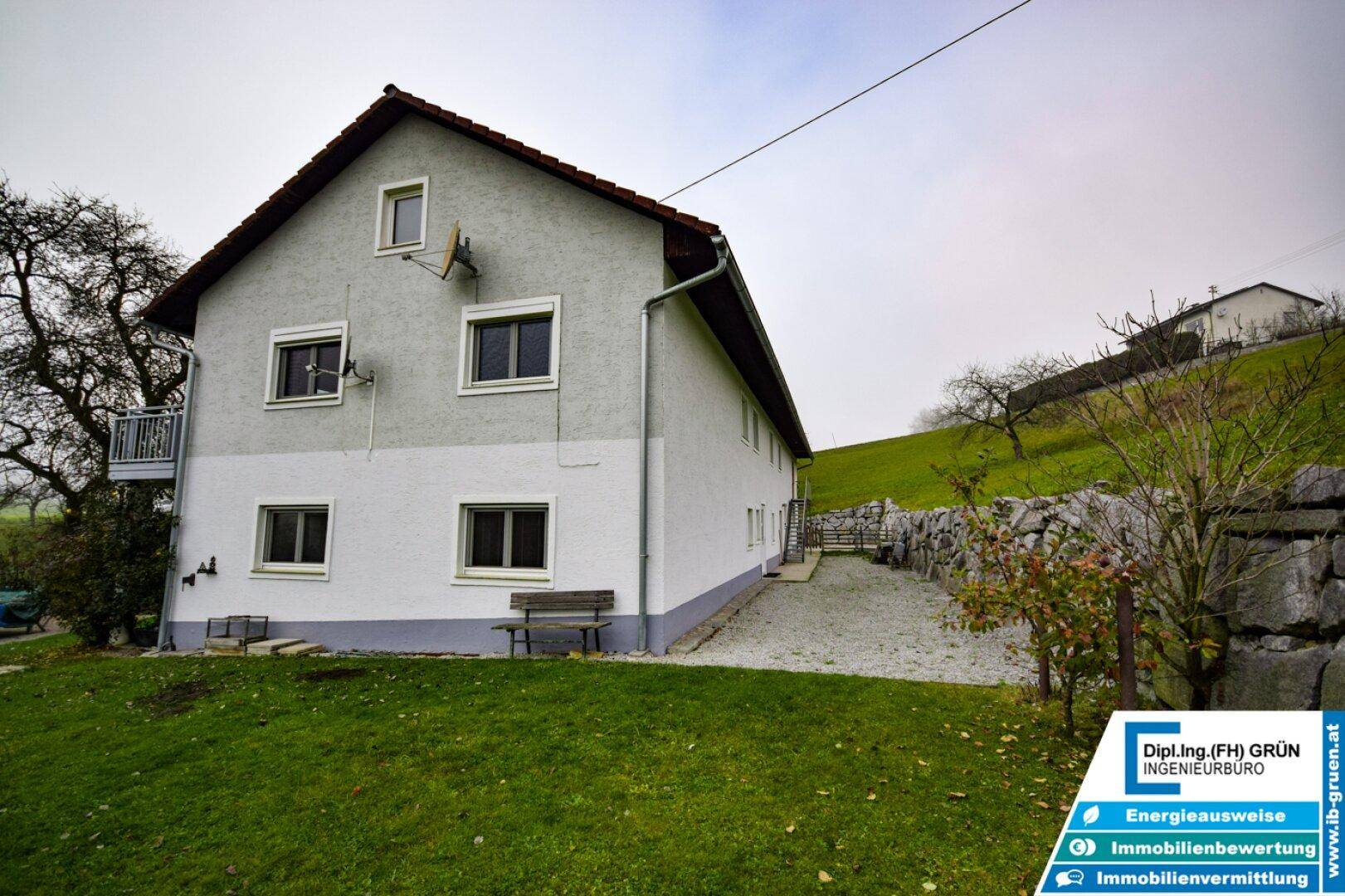 Seitenansicht des Wohnhauses mit weißer Fassade, Fenstern und einem kleinen Balkon.