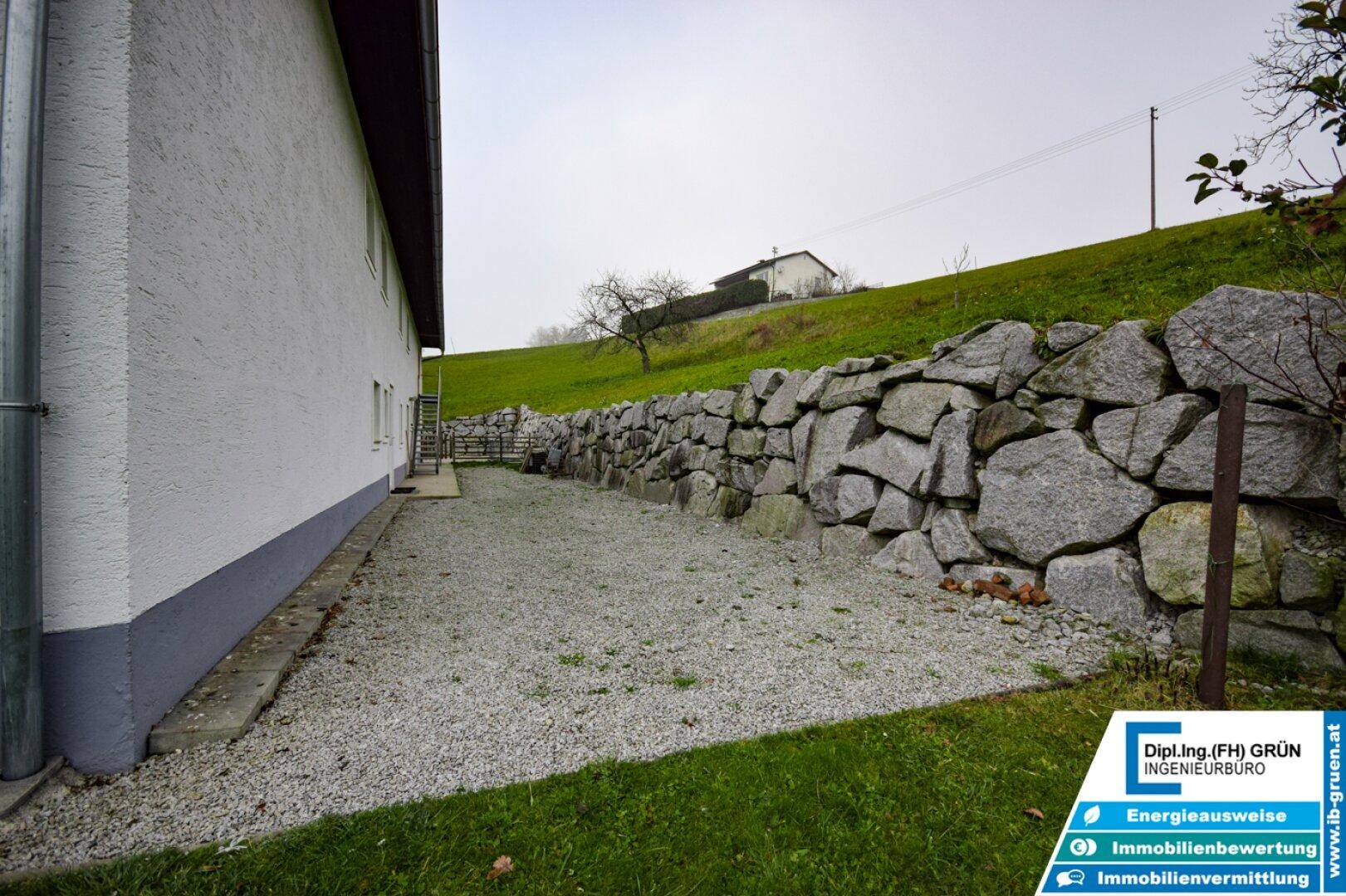 Seitenbereich des Hauses mit einer robusten Natursteinmauer und einem Schotterweg.