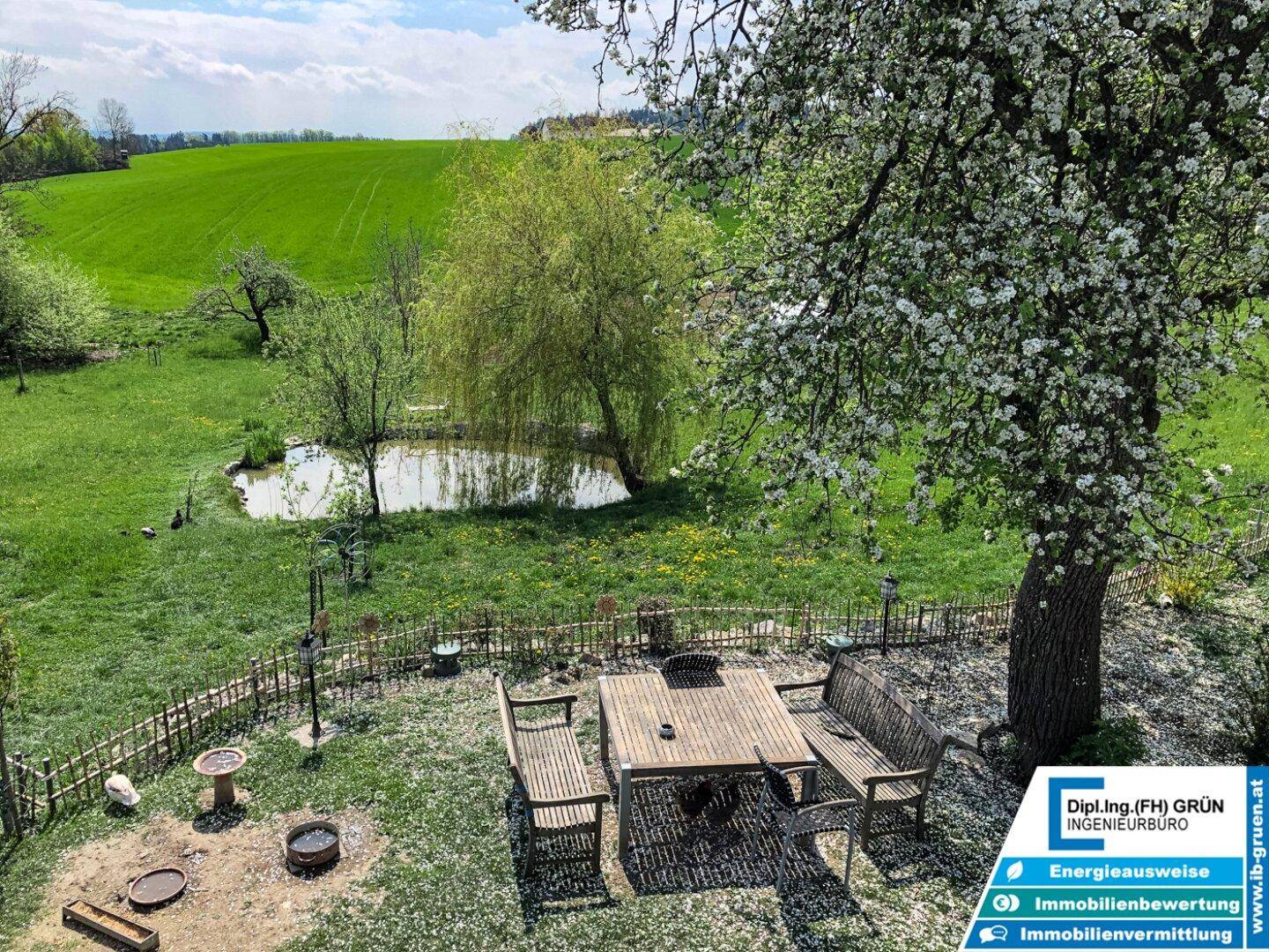 Idyllischer Essbereich im Freien mit Holztisch und Bänken, Blick auf einen Teich.