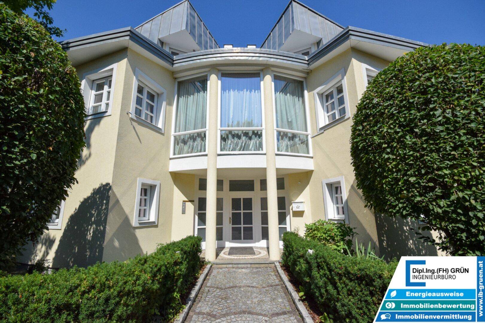 Die repräsentative Frontansicht des Hauses mit großen Fenstern und gepflegter Bepflanzung unter strahlend blauem Himmel.