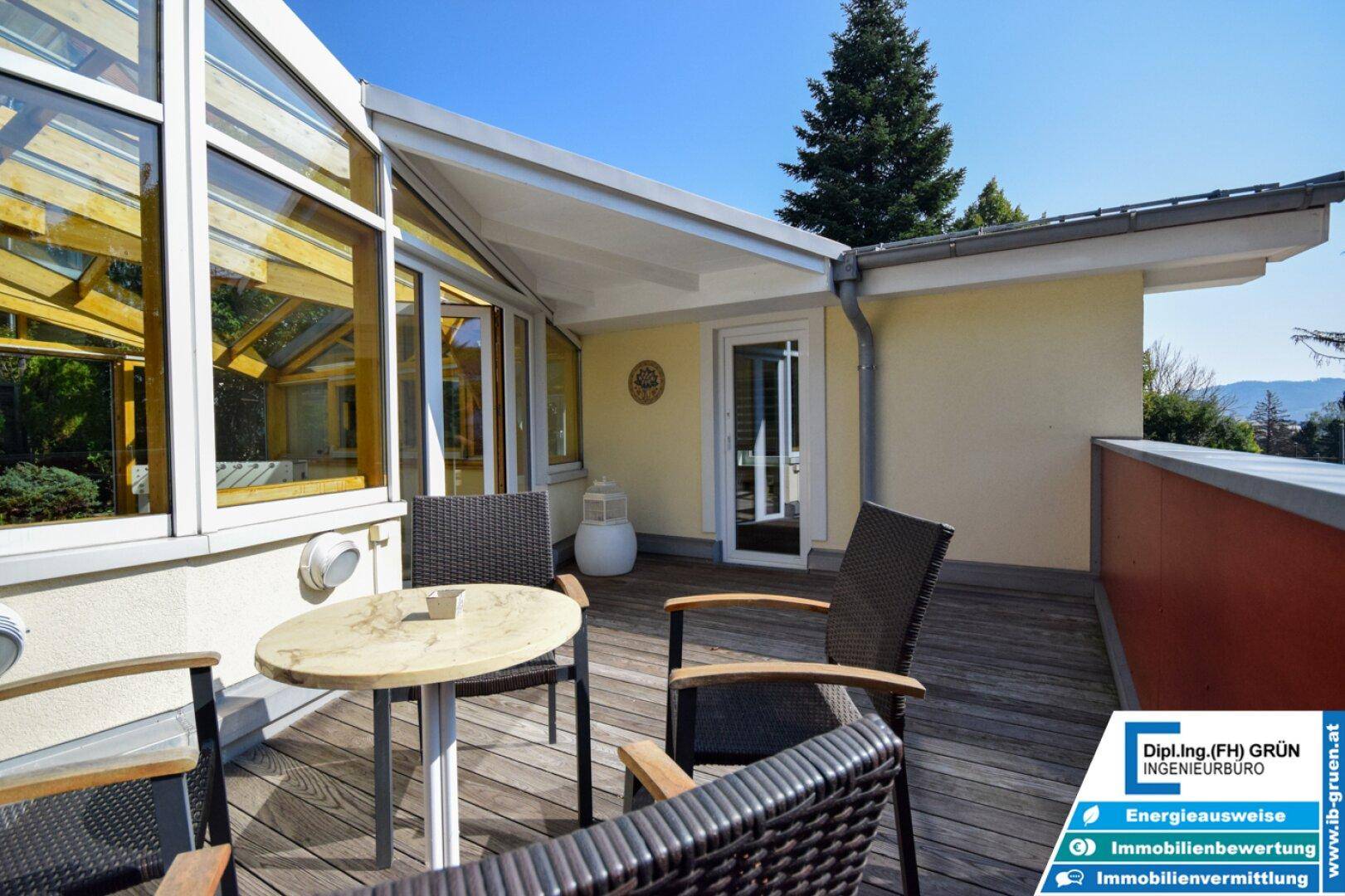 Sonniger Terrassenbereich mit Holzboden, Sitzgelegenheiten und Zugang zum Wintergarten.