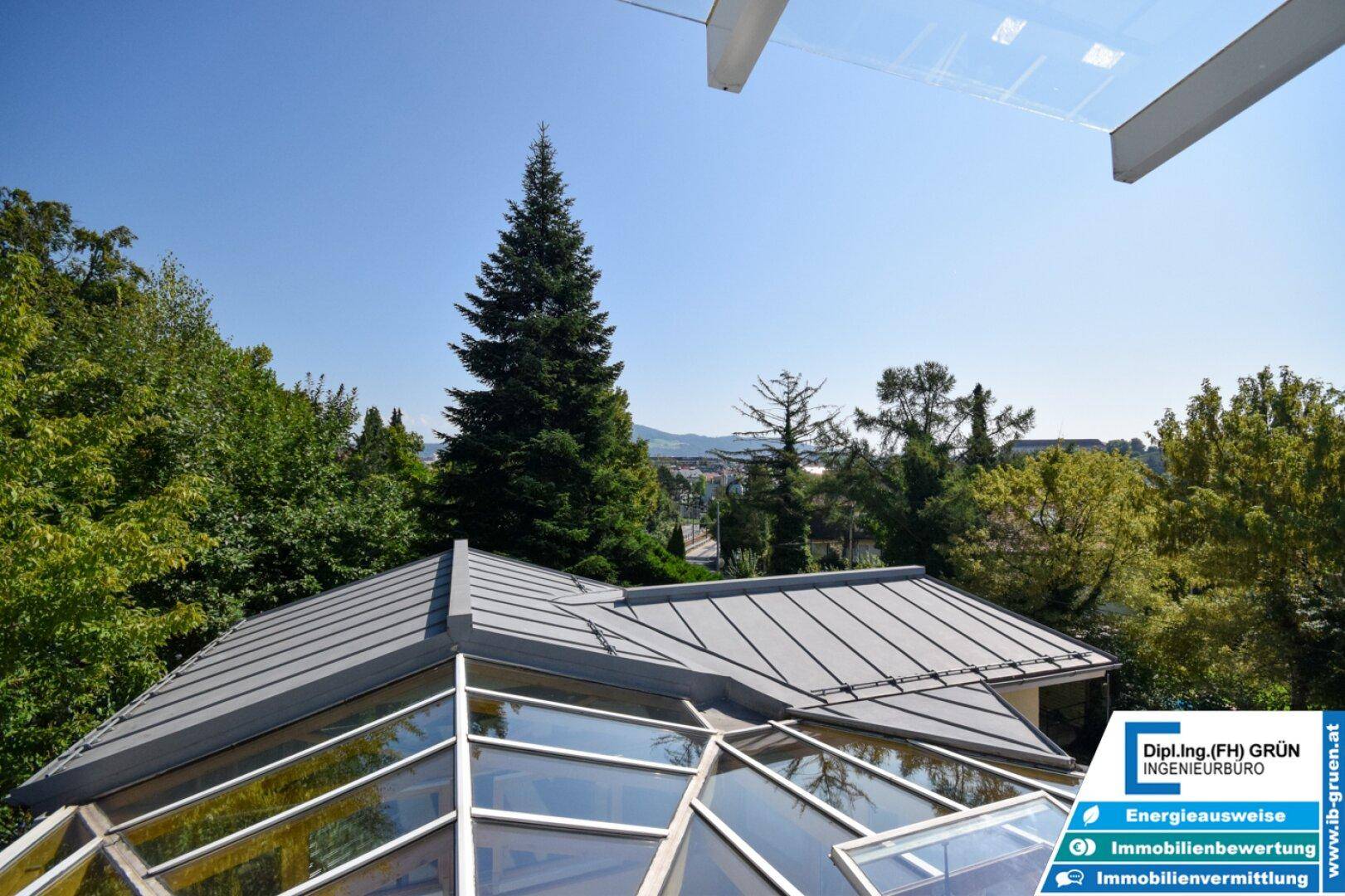 Blick über das Dach des Wintergartens auf die umliegende grüne Landschaft und entfernte Berge.