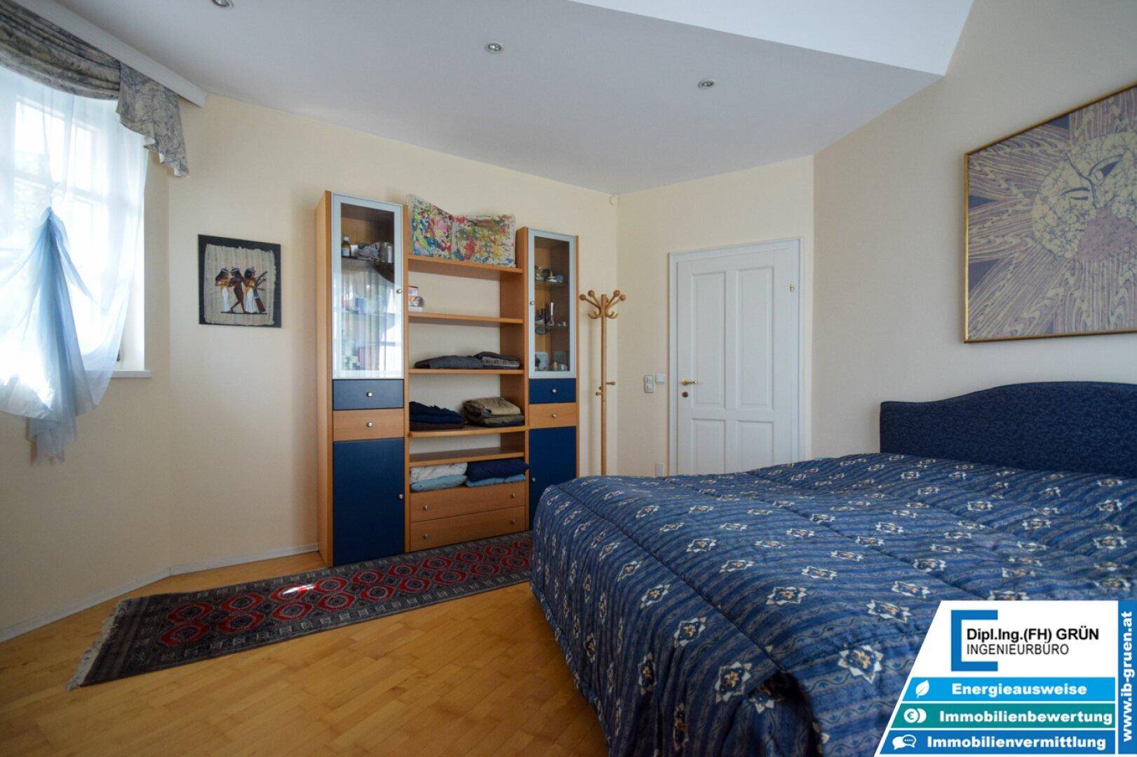 Schlafzimmer mit Parkettboden, blauem Bett und einem Schrank mit viel Stauraum.