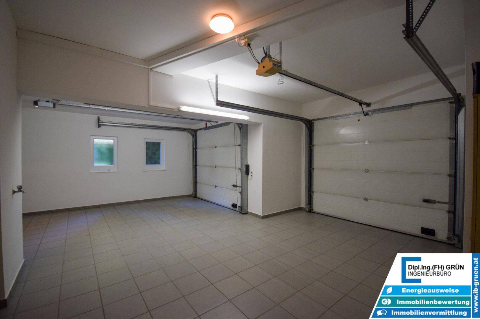Geräumige Doppelgarage mit Fliesenboden, zwei Toren und Fenstern für ausreichend Licht.