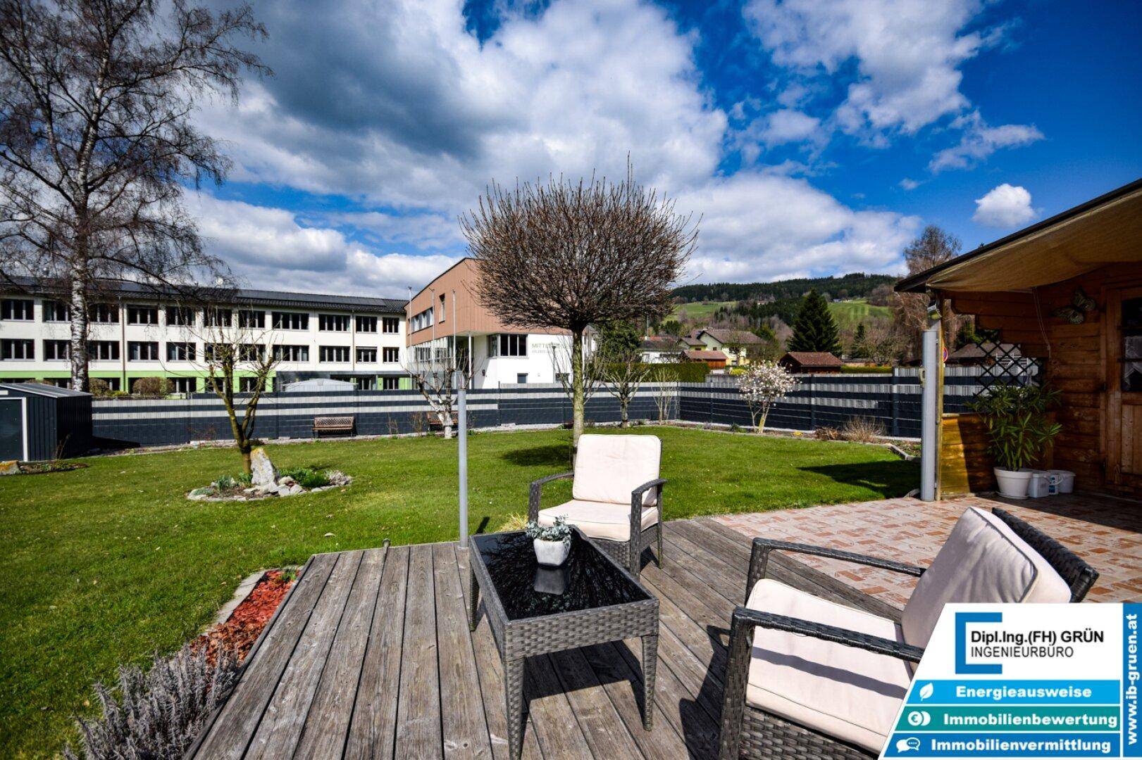 Gemütliche Holzterrasse mit Rattanmöbeln und Blick auf den grünen Garten und die Umgebung.