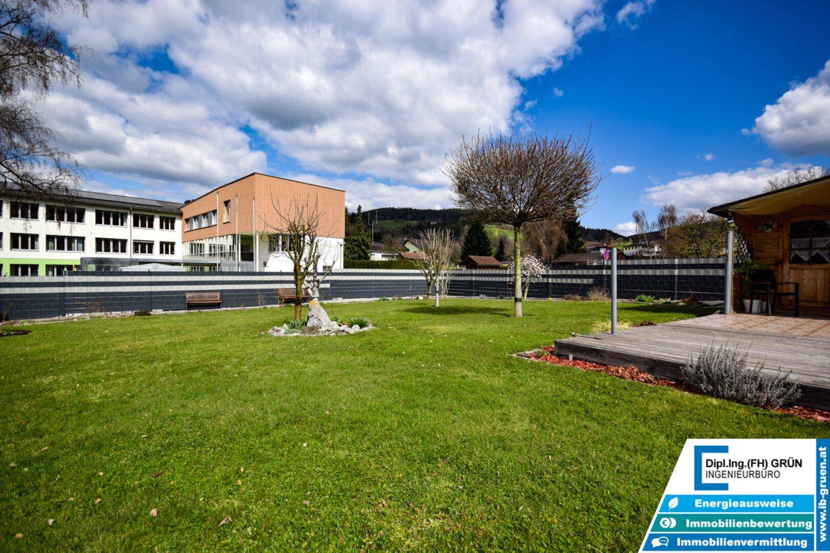Panoramablick über den grünen Garten mit Holzterrasse und dem angrenzenden Gebäude.