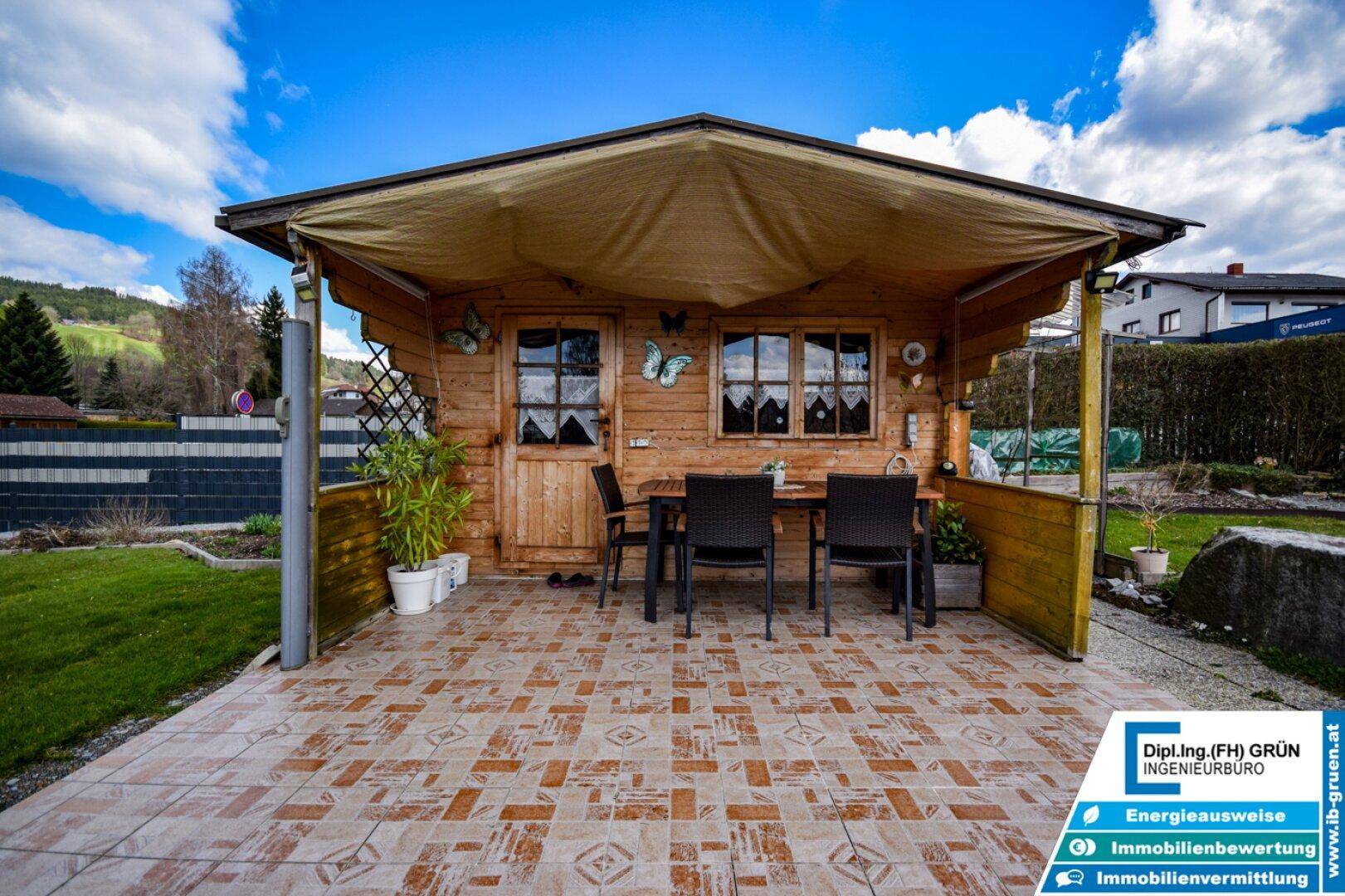 Überdachte Terrasse vor dem Gartenhaus mit Fliesenboden und einem Esstisch im Freien.