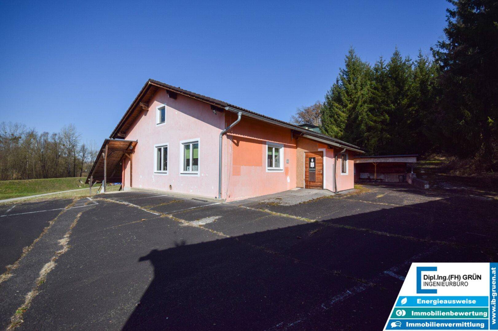 Seitenansicht eines Gebäudes mit hellrosa Fassade, mehreren Fenstern und einem kleinen überdachten Eingangsbereich.
