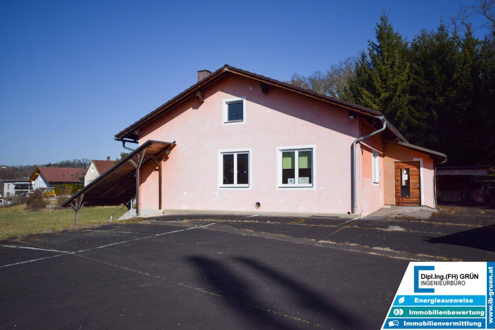 Seitenansicht eines Gebäudes mit hellrosa Fassade, mehreren Fenstern und einem kleinen Vordach.