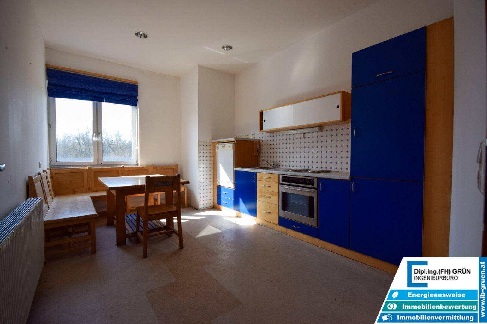 Küche mit blauen und holzfarbenen Schränken, einem Esstisch und einem Fenster mit blauer Jalousie.