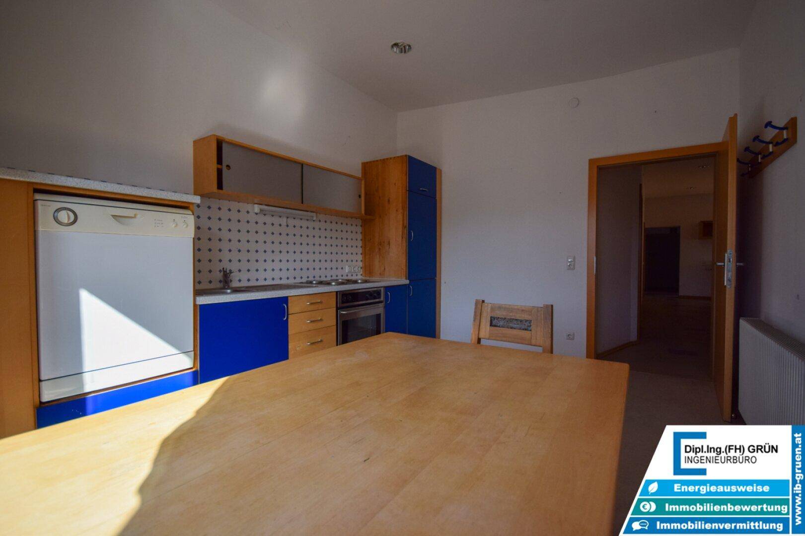Küche mit eingebautem Geschirrspüler, blauen und holzfarbenen Schränken und einem großen Holztisch.