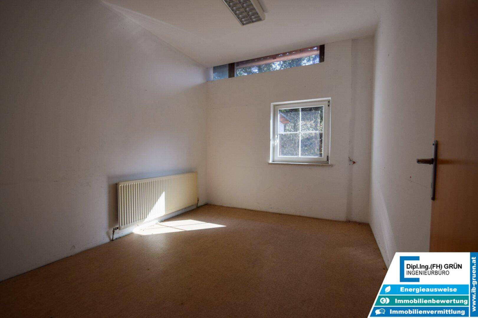 Kleiner, leerer Raum mit Teppichboden, einem Fenster und einem Heizkörper, einfach und funktional.