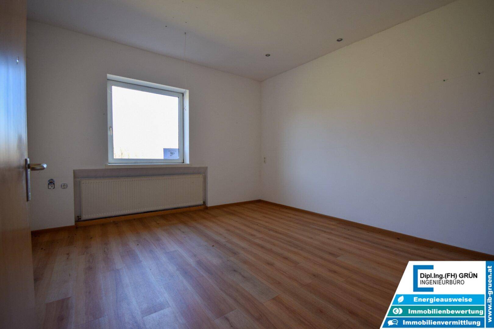 Helles Zimmer mit Laminatboden und einem Fenster, das viel natürliches Licht hereinlässt.