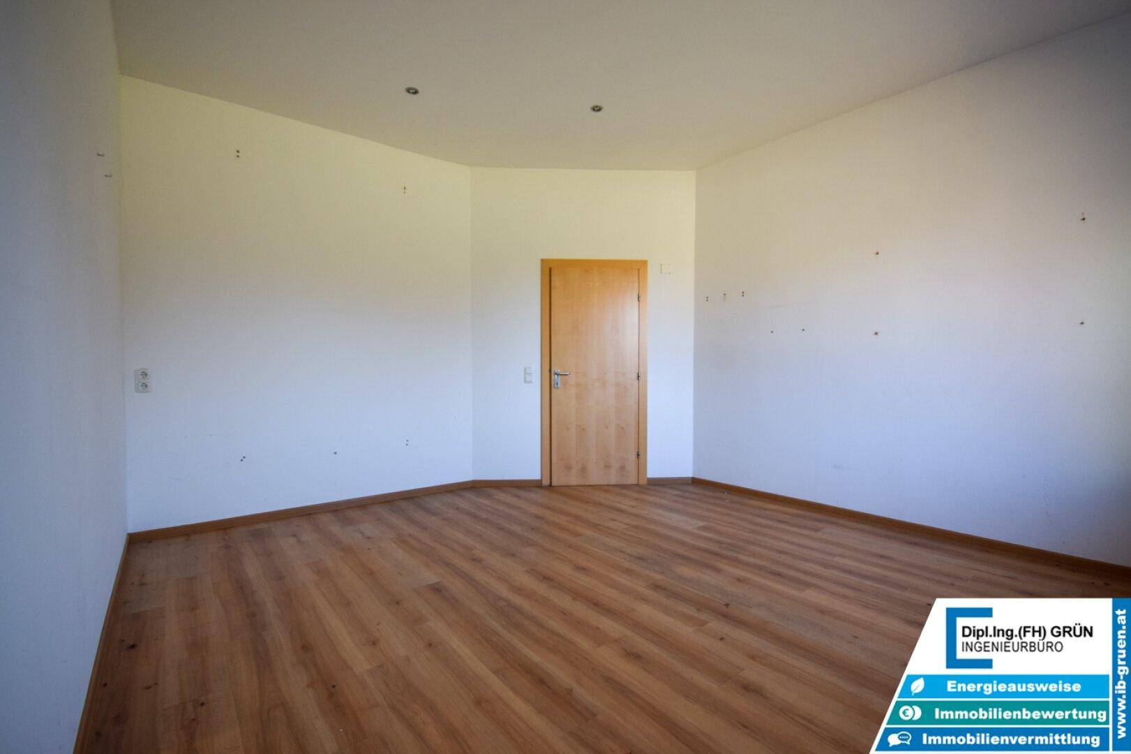 Leeres Zimmer mit Laminatboden und einer Holztür, bereit für die individuelle Gestaltung.