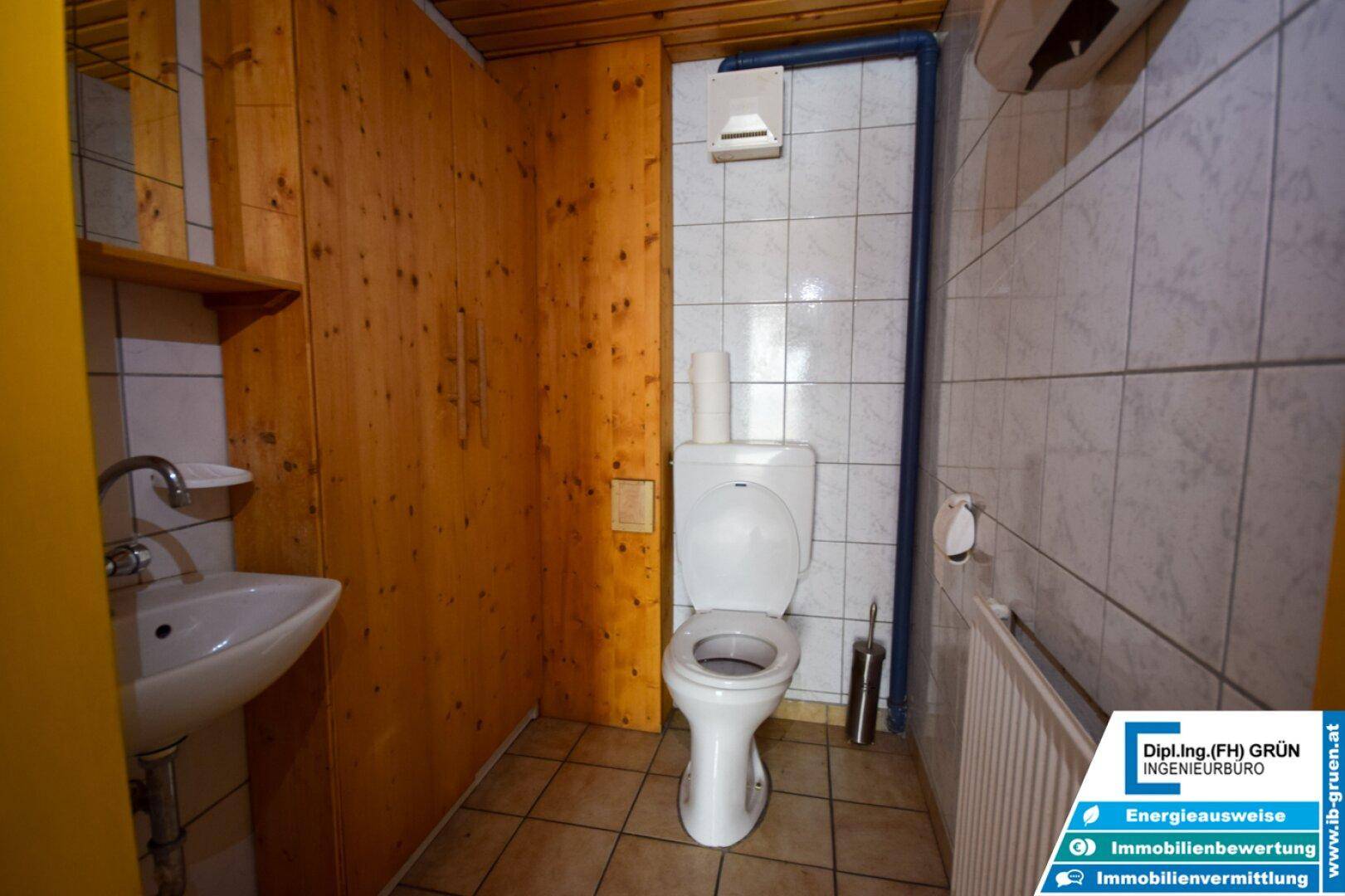 Einfache Toilette mit Fliesenboden, Waschbecken und Holzverkleidung an den Wänden.
