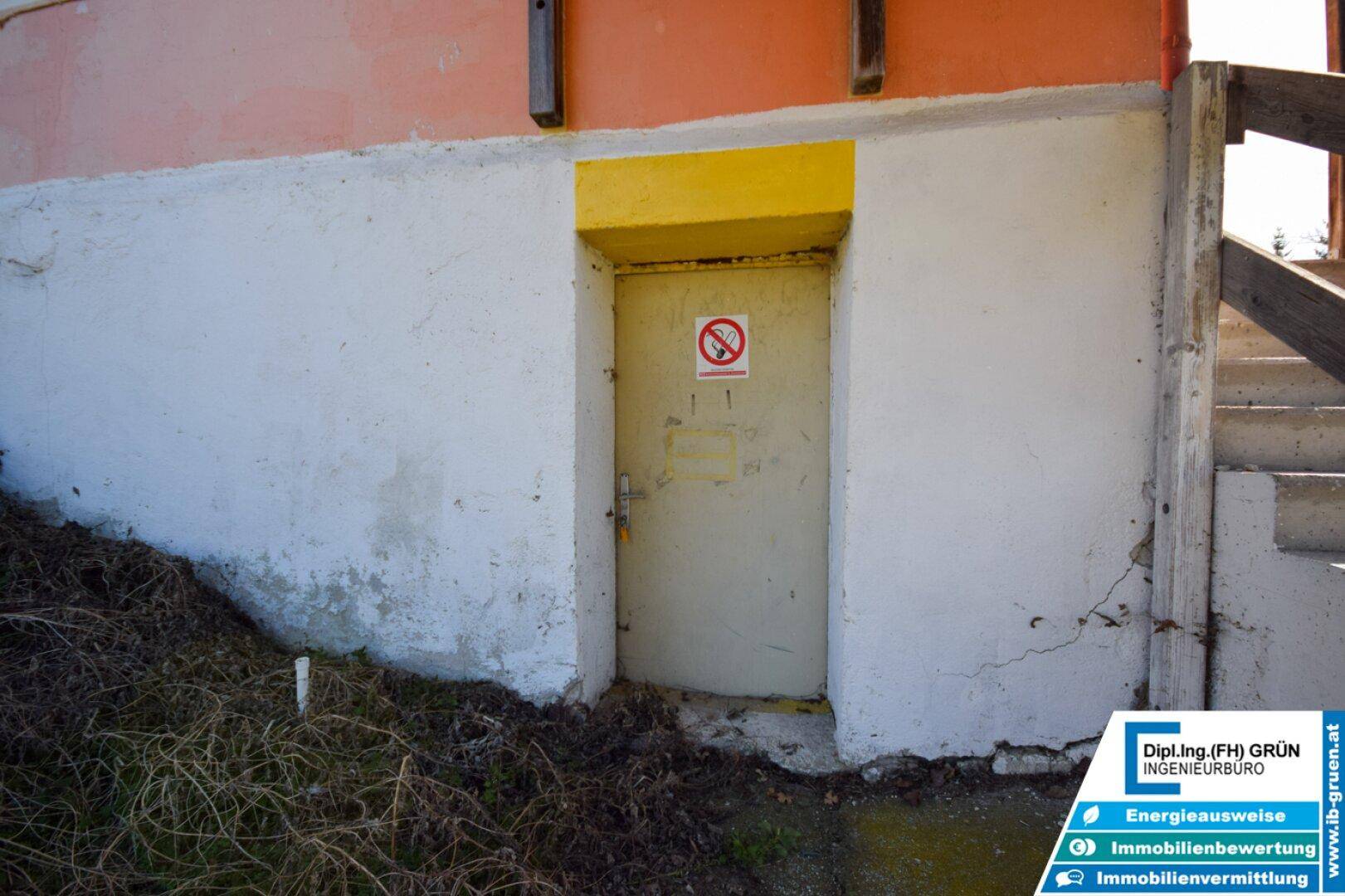 Eingang zum Kellerbereich mit einer einfachen Tür und einer Treppe, umgeben von Betonwänden.