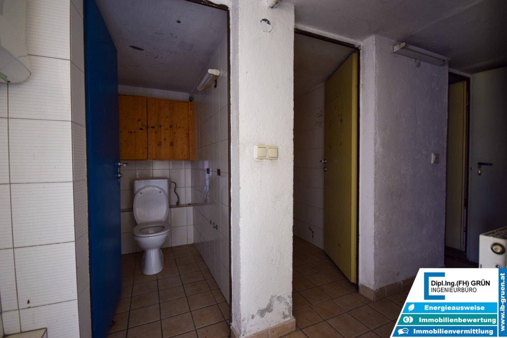 Zwei Toilettenkabinen mit Fliesenboden und einfachen Holzschränken in einem Sanitärbereich.