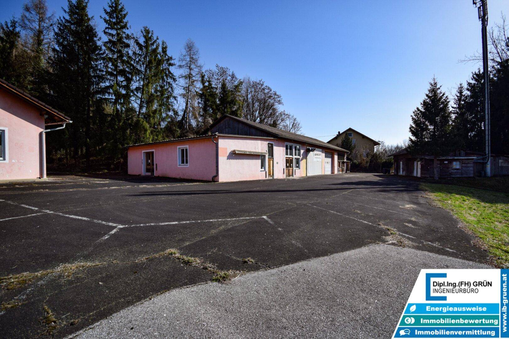 Weitläufiger asphaltierter Parkplatz vor mehreren rosa Gebäuden, umgeben von Bäumen und Natur.