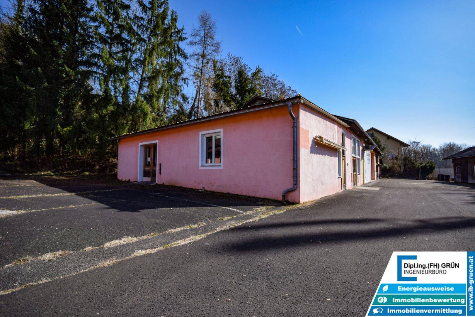 Seitenansicht eines rosa Gebäudes mit Fenstern und einem großen asphaltierten Bereich davor.