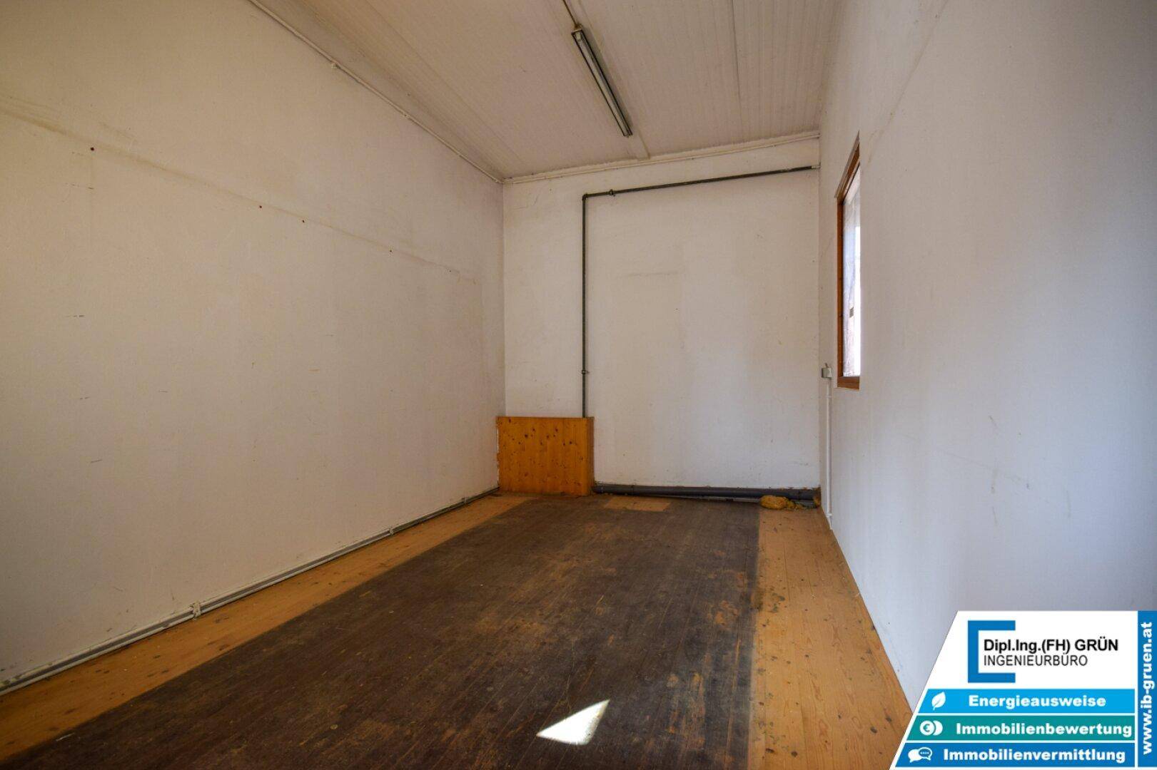 Langer, schmaler Raum mit Holzboden und einem Fenster, ideal als Abstell- oder Arbeitsbereich.