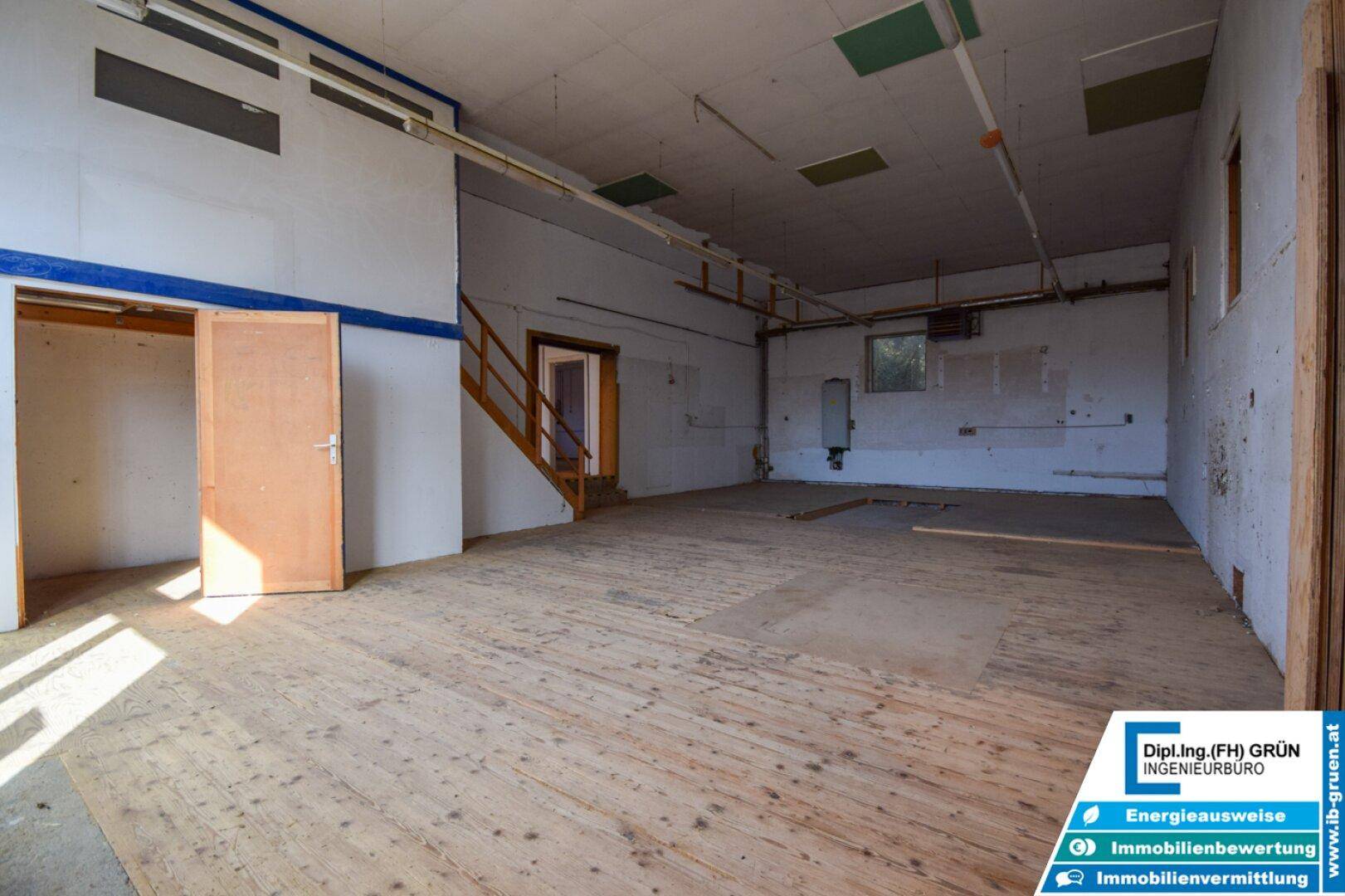 Große Halle mit Holzboden, Treppe und sichtbaren Wänden, ideal für Lager oder Werkstatt.