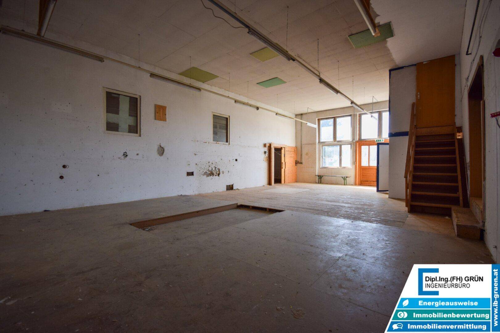 Großer, leerer Lagerraum mit Betonboden, hohen Decken und Tageslicht durch Fenster.