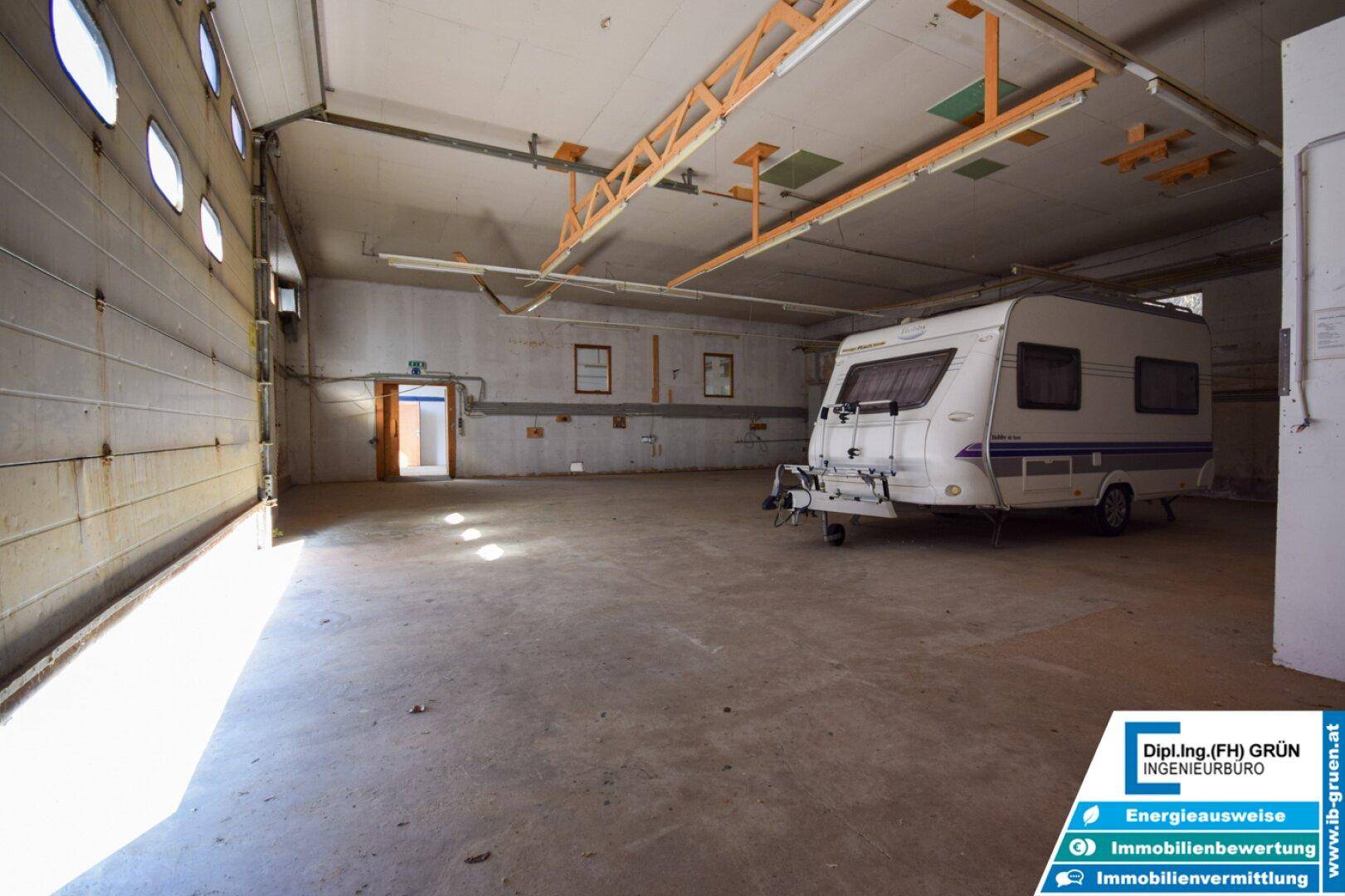 Geräumiger Lagerraum mit Rolltor, Betonboden und einem geparkten Wohnwagen.