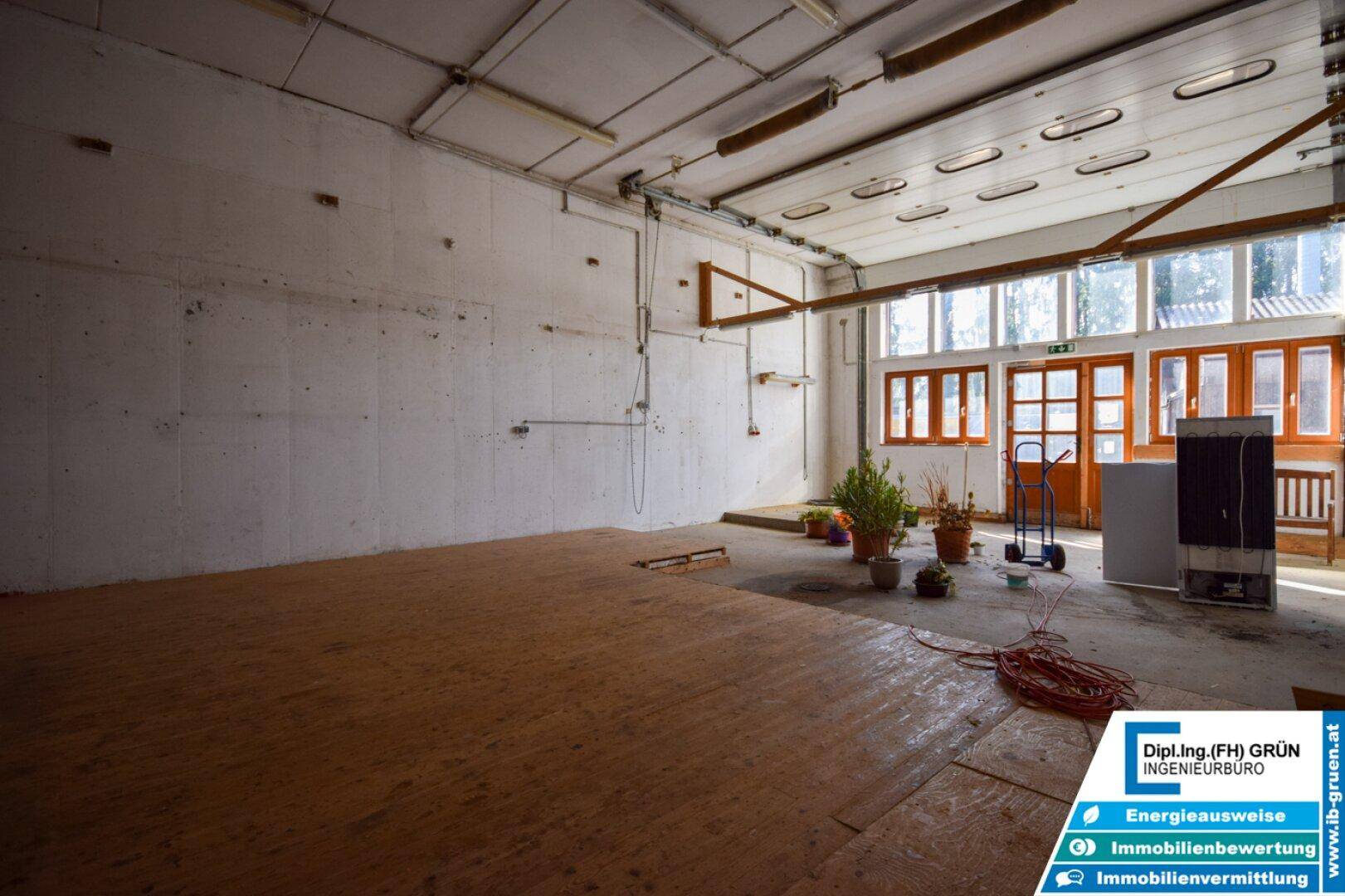 Großer, heller Lagerraum mit Holzboden, hohen Decken und Pflanzen am Fensterbereich.