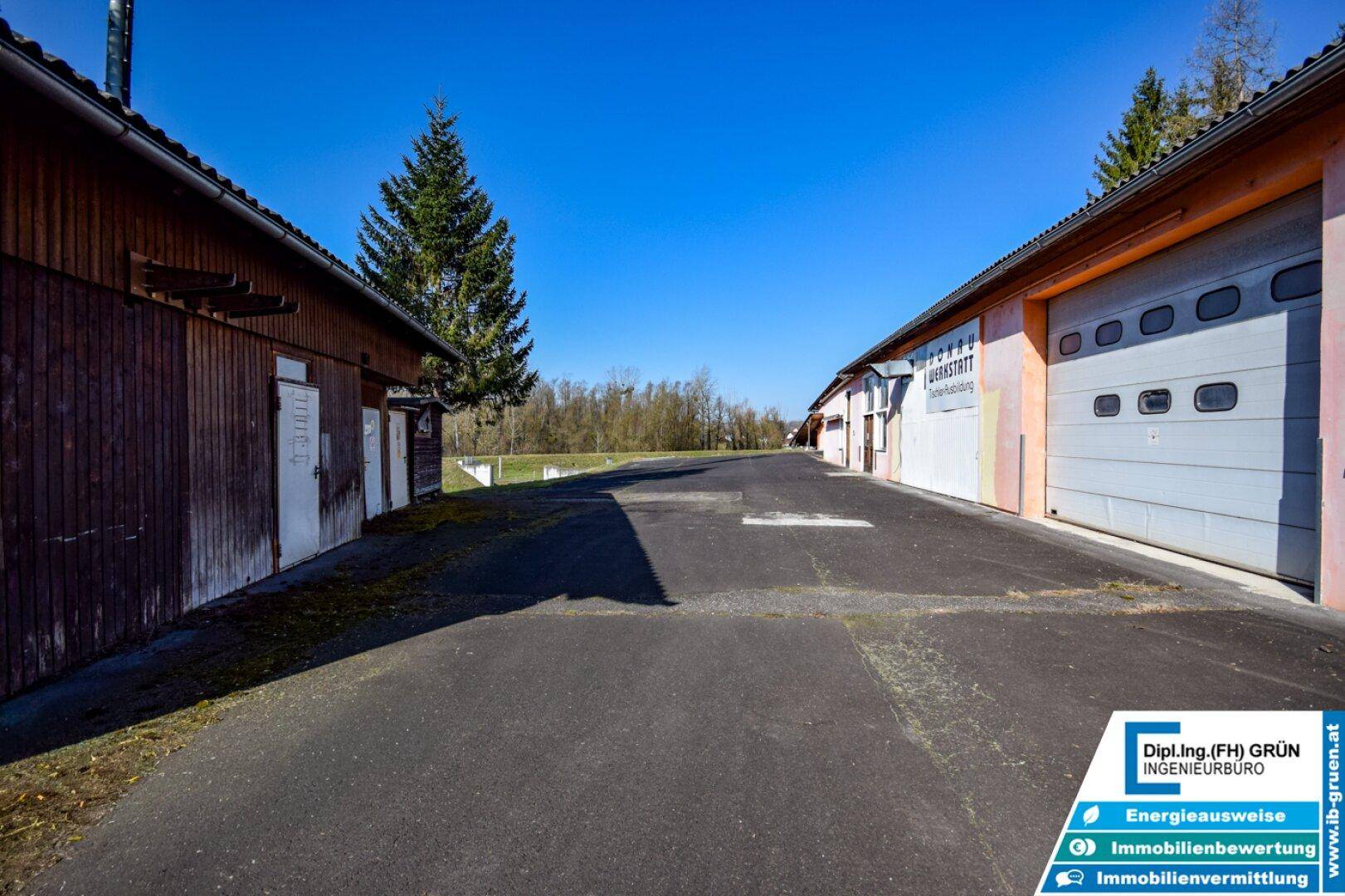 Lange Zufahrt zwischen Lagerhallen mit Garagentoren unter blauem Himmel.