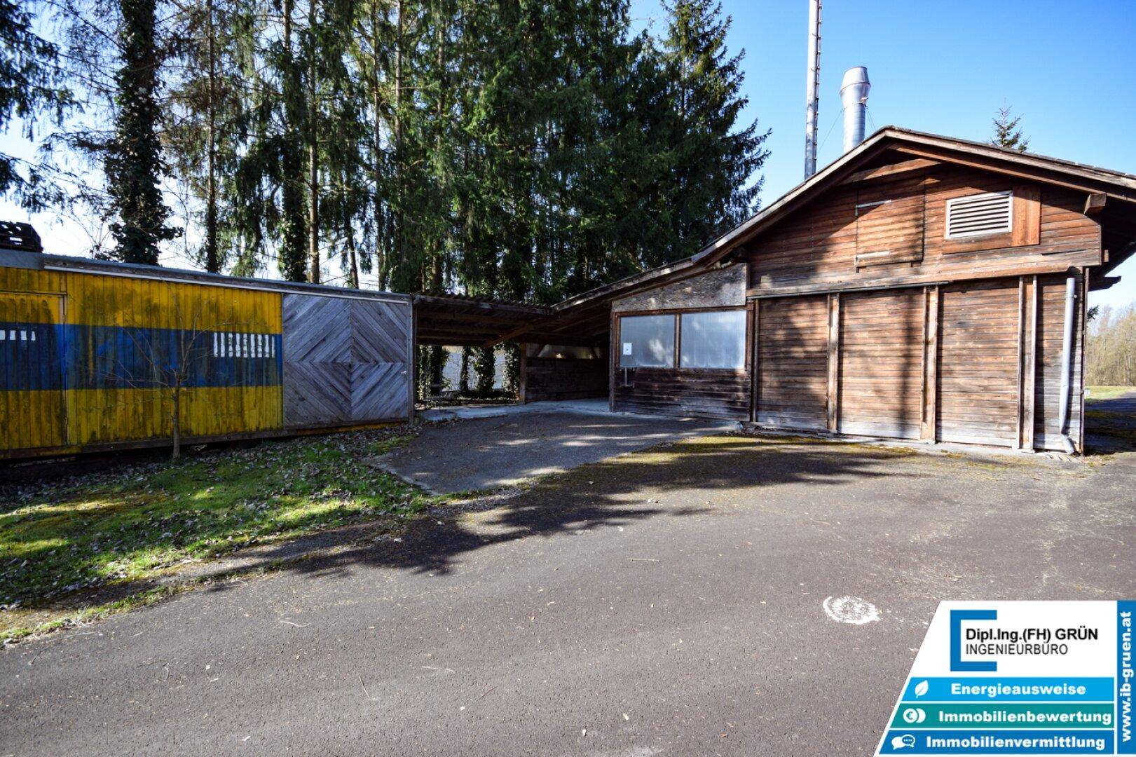 Mehrere Gebäude mit Holzwänden und einem überdachten Bereich unter Bäumen.