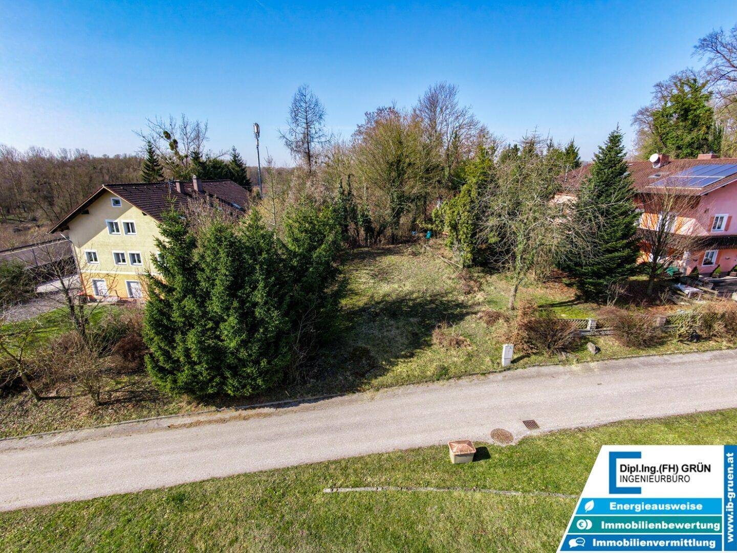 Blick auf das unbebaute Grundstück mit Grasfläche, Bäumen und angrenzenden Wohnhäusern.