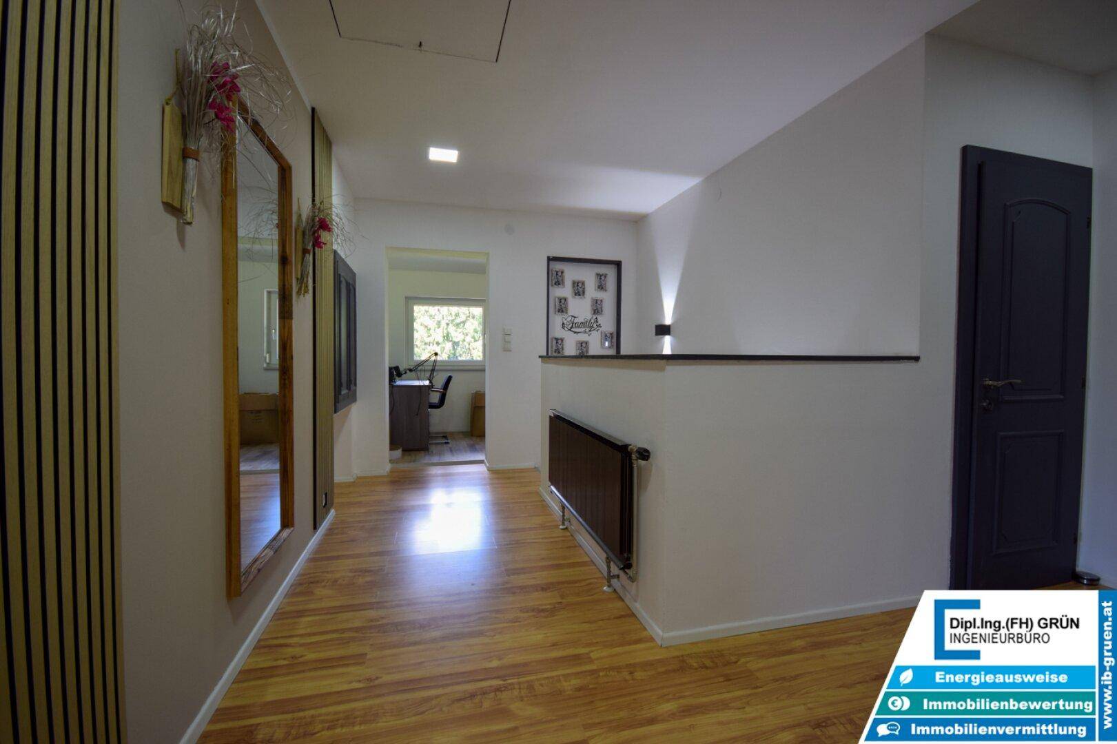 Heller Flur mit Holzfußboden, großem Spiegel und Blick in ein angrenzendes Arbeitszimmer.