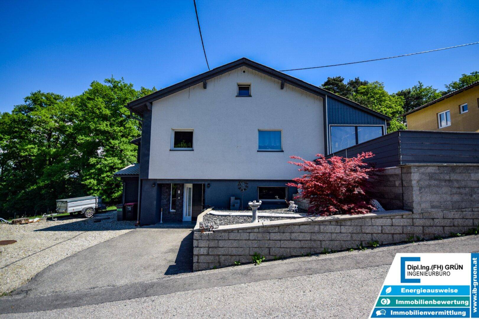 Modernes Einfamilienhaus mit weißer und anthrazitfarbener Fassade und gepflegtem Vorgartenbereich.
