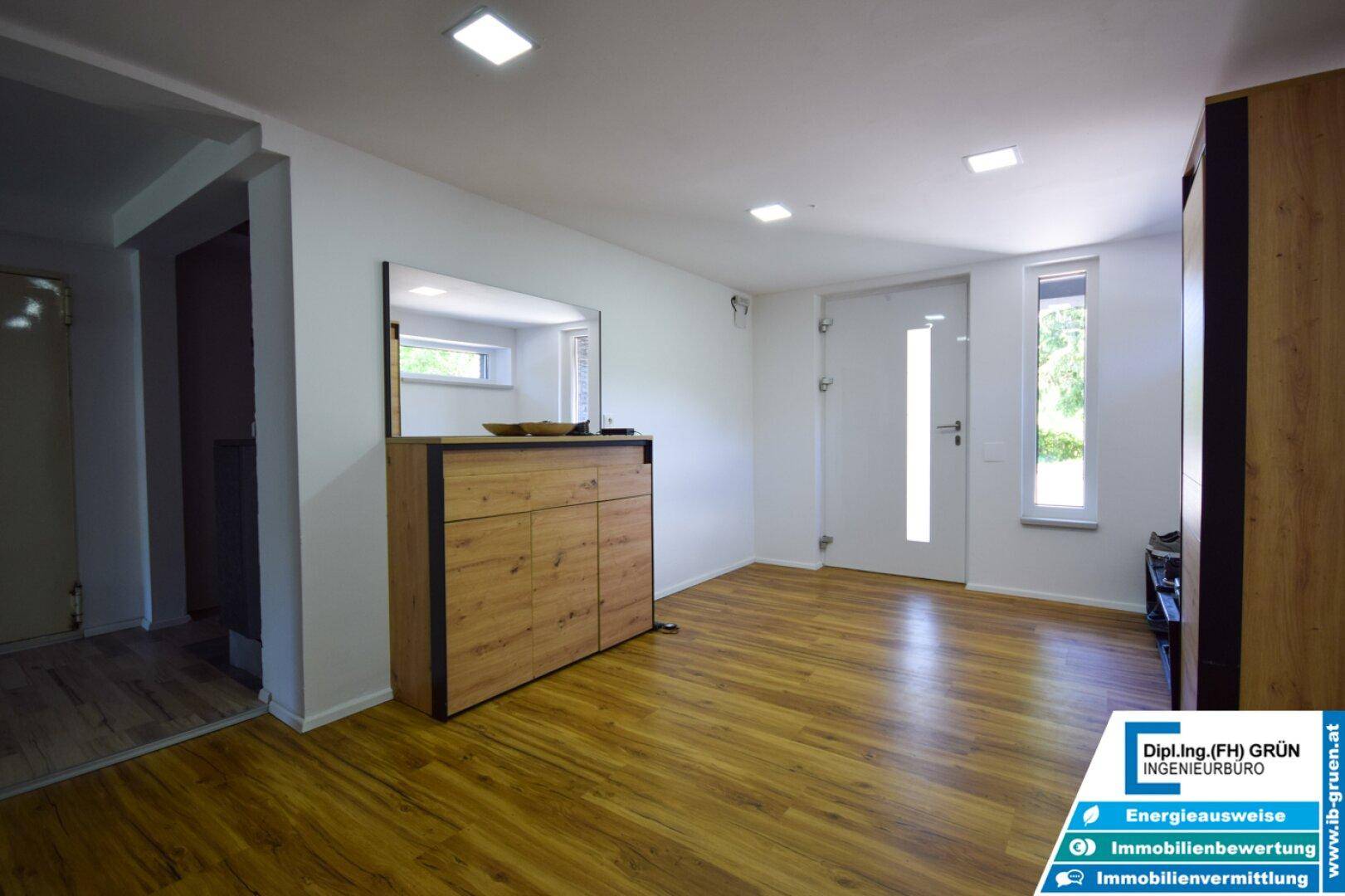 Heller Eingangsbereich mit Holzfußboden, Spiegel und moderner Kommode in Holzoptik.