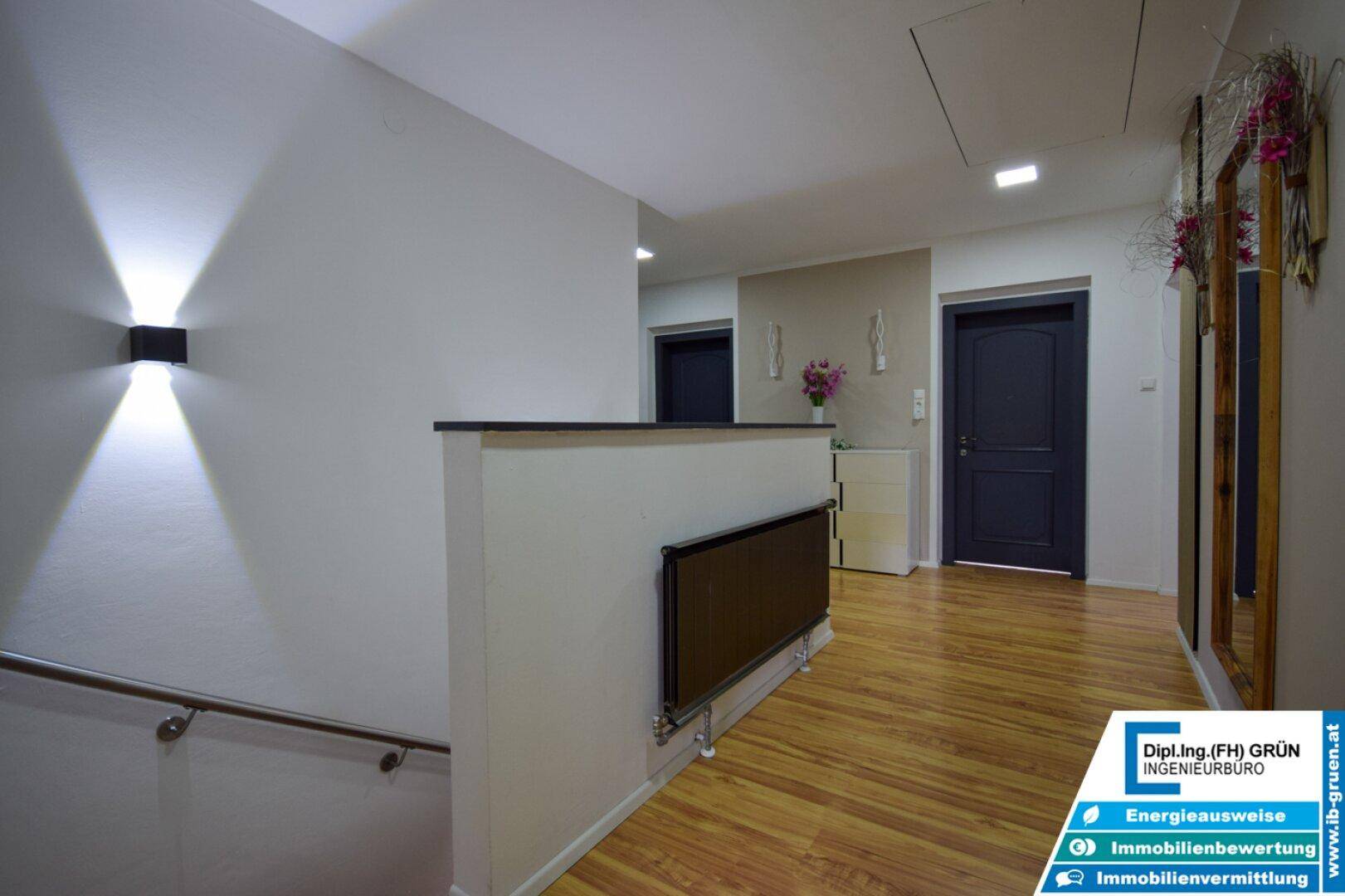 Heller Flur mit Holzfußboden, Treppenaufgang und modernem Heizkörper an der Wand.