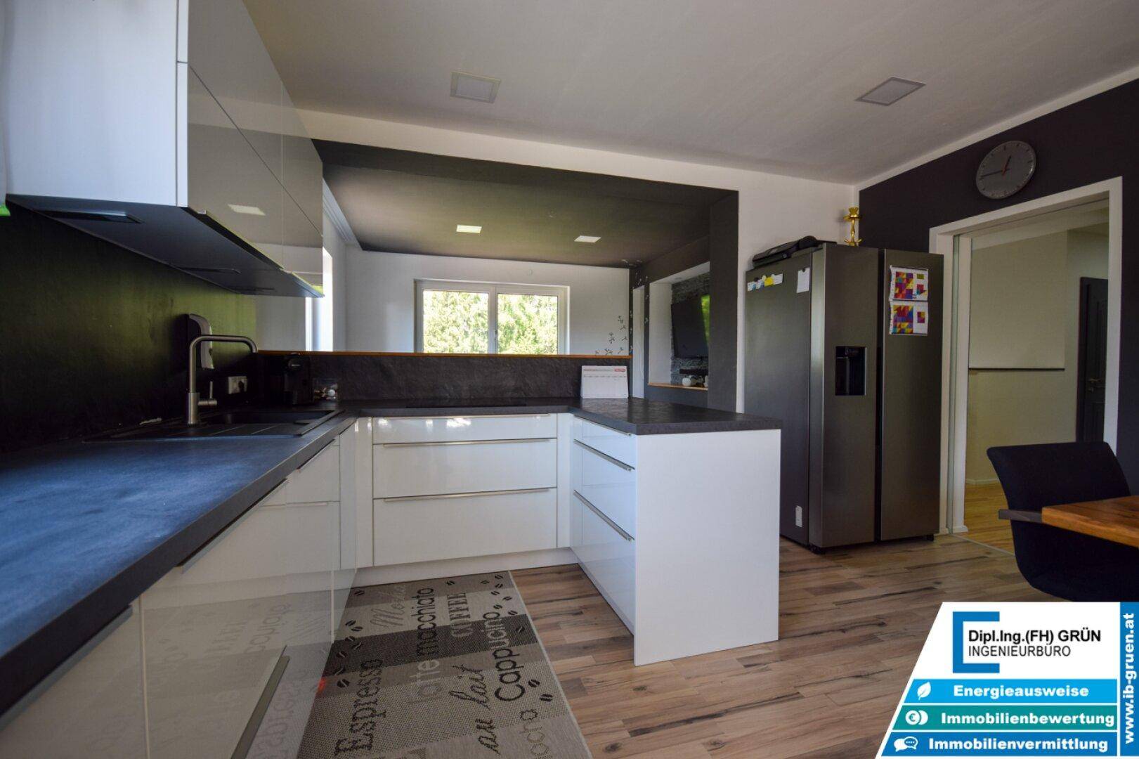 Funktionale Küche mit weißen Schränken, dunklen Arbeitsplatten und großem Side-by-Side Kühlschrank.