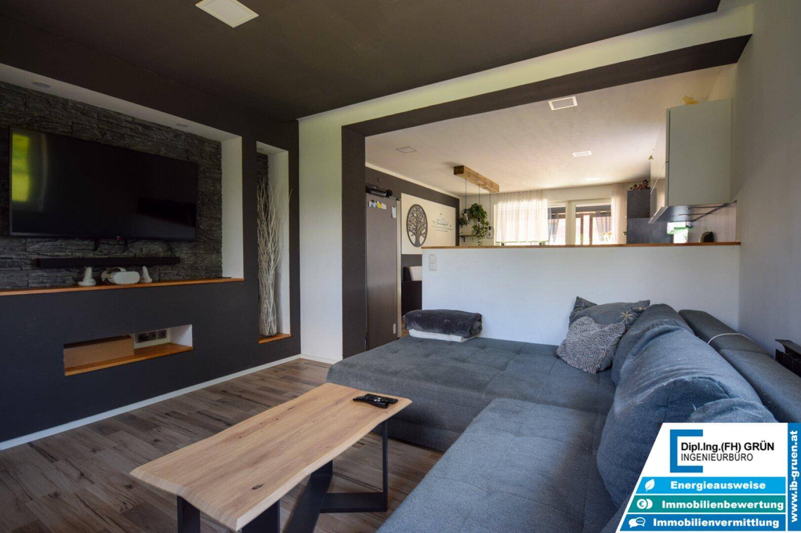 Offener Wohnbereich mit Sofa und Blick auf die angrenzende Küche, getrennt durch eine Halbwand.