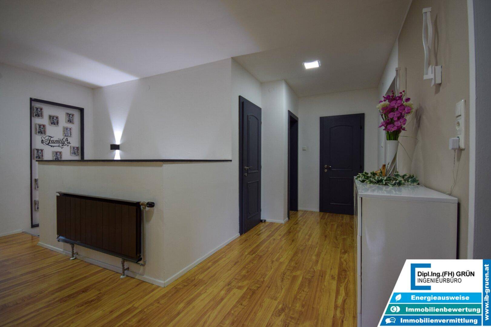 Heller Flur mit Holzfußboden, Treppenaufgang und modernem Heizkörper an der Wand.