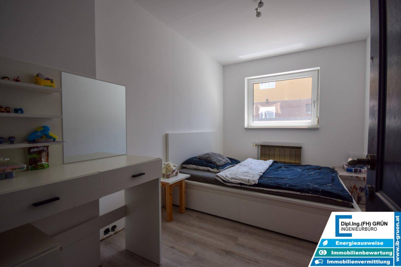 Helles Schlafzimmer mit Holzboden, weißem Bett und einem Schreibtisch mit Spiegel.
