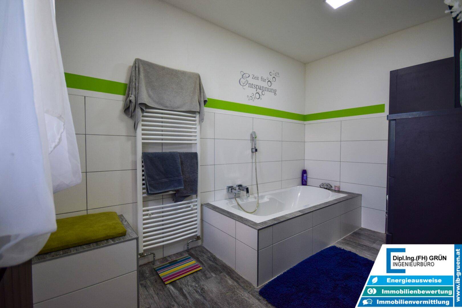 Badezimmer mit Badewanne, Handtuchheizkörper und grünen Farbakzenten an den Wänden.