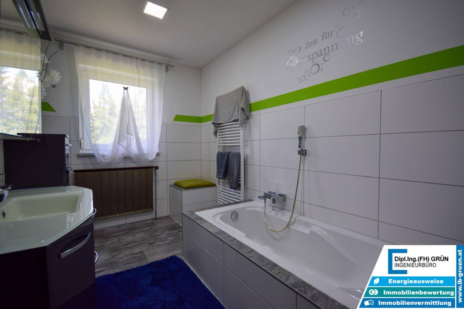 Modernes Badezimmer mit Badewanne, grünen Akzenten und einem Fenster für Tageslicht.