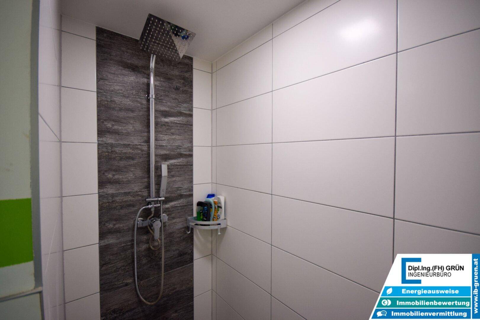 Duschbereich mit Regendusche und modernen Fliesen in Weiß und dunklem Grau.