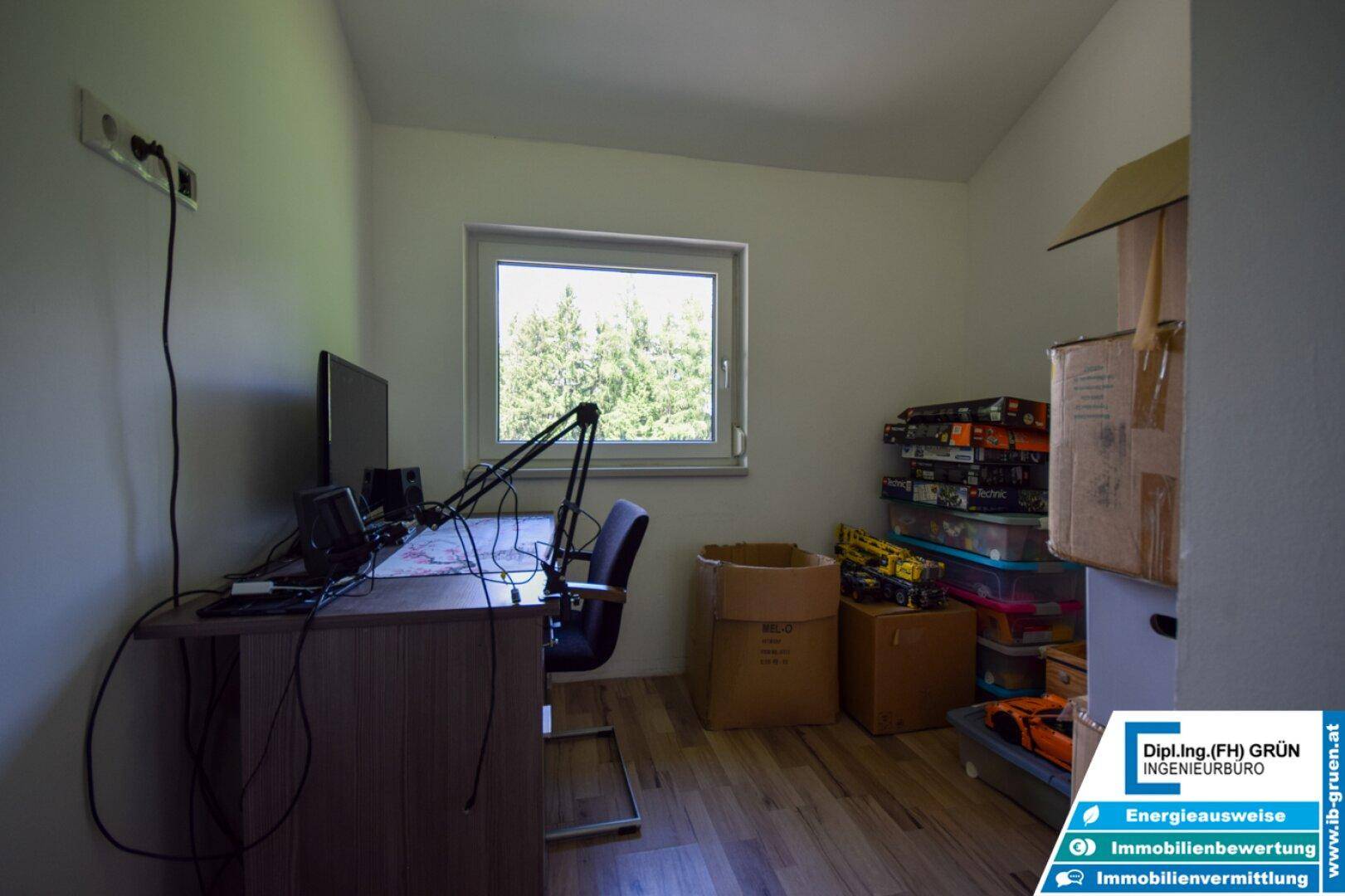 Arbeitszimmer mit Schreibtisch, Computer und Blick ins Grüne durch das Fenster.