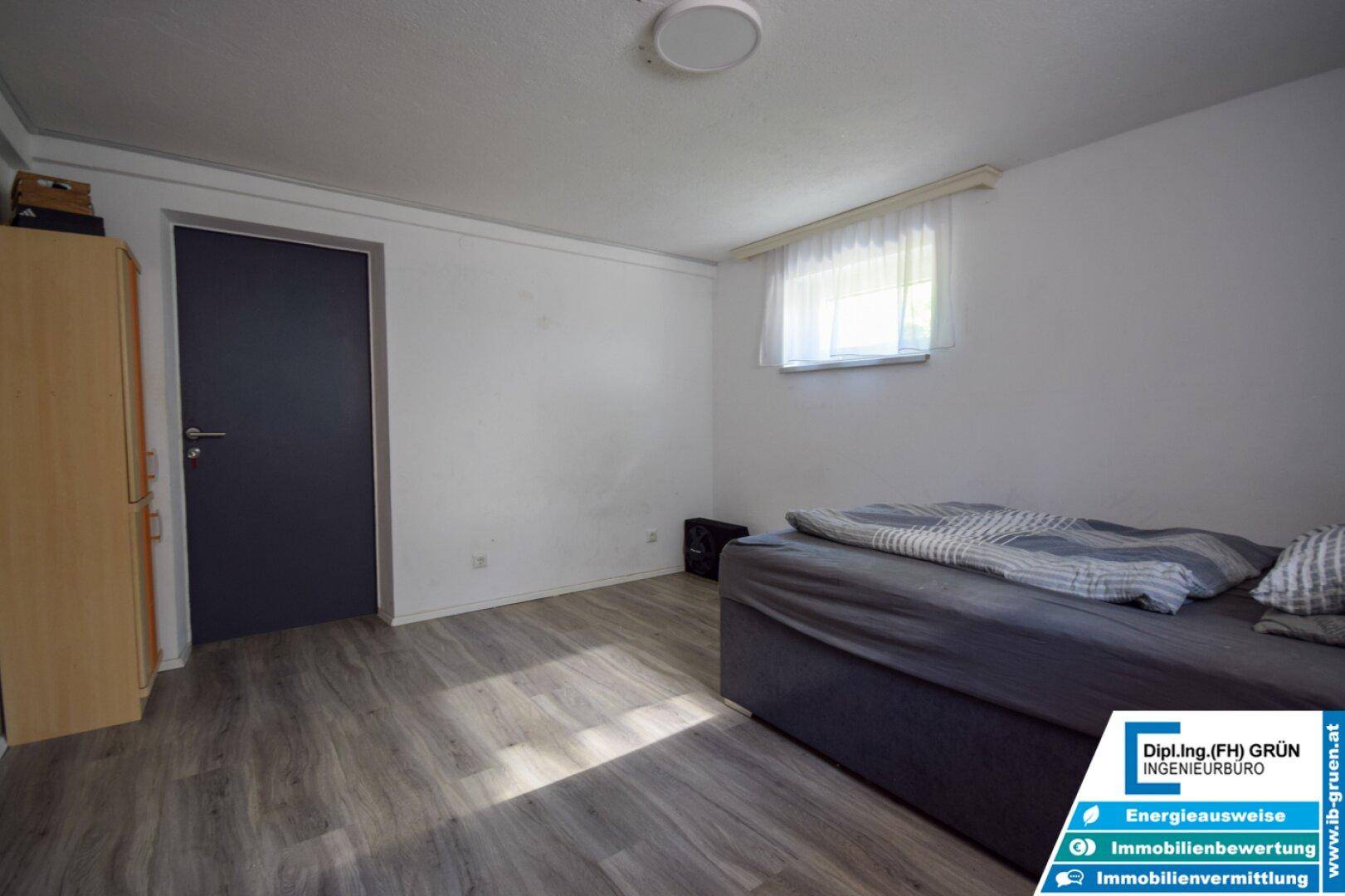 Schlafzimmer im Untergeschoss mit Holzboden und dunkler Tür, bereit zur Einrichtung.