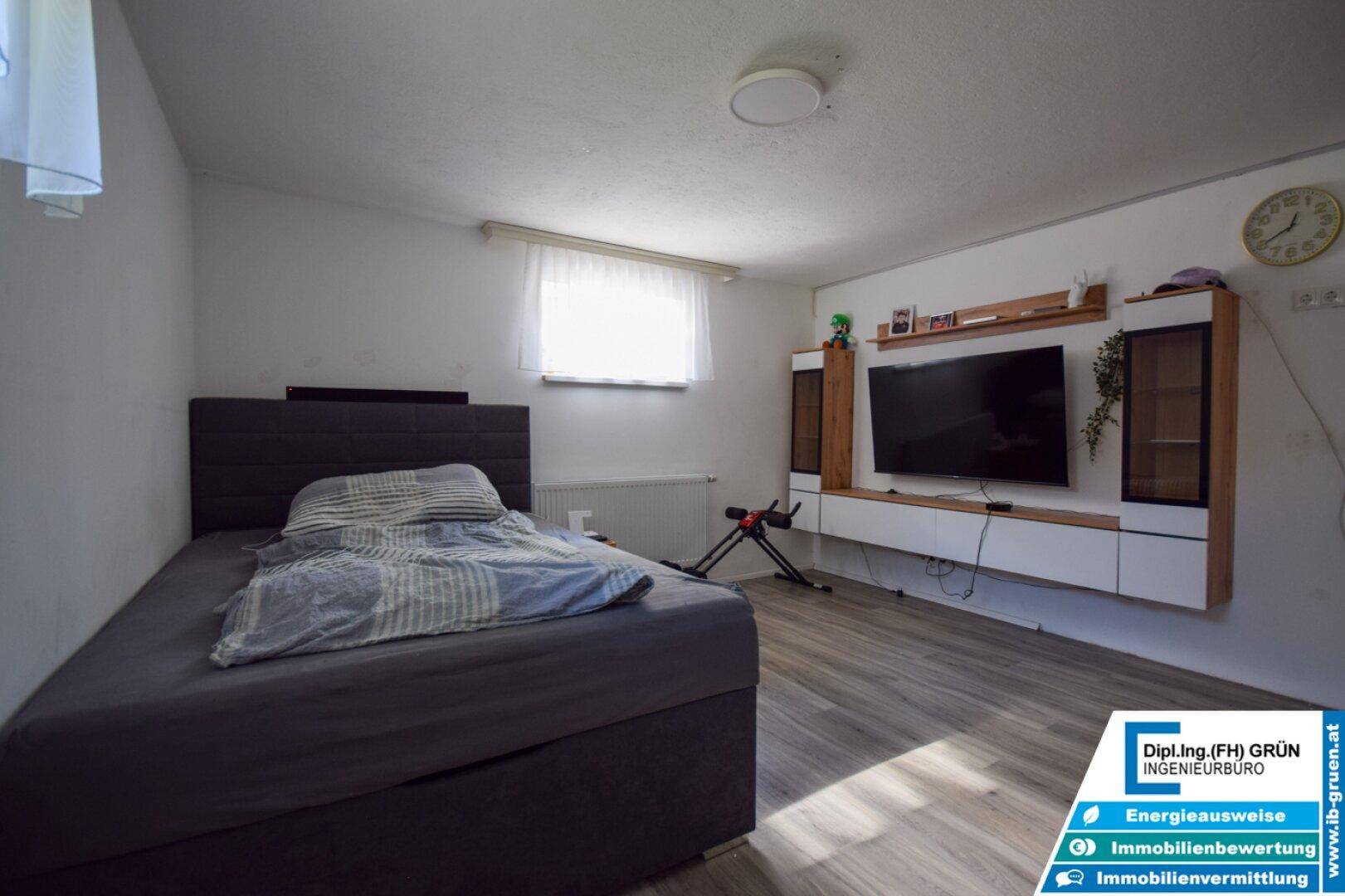 Schlafzimmer im Untergeschoss mit Bett, TV-Möbel und viel Tageslicht.