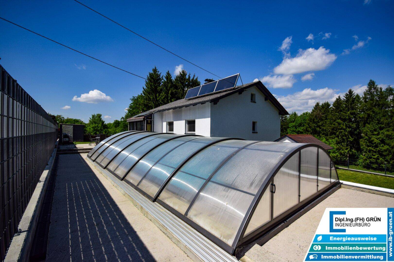 Haus mit überdachtem Pool, Solaranlage auf dem Dach und viel Grün.