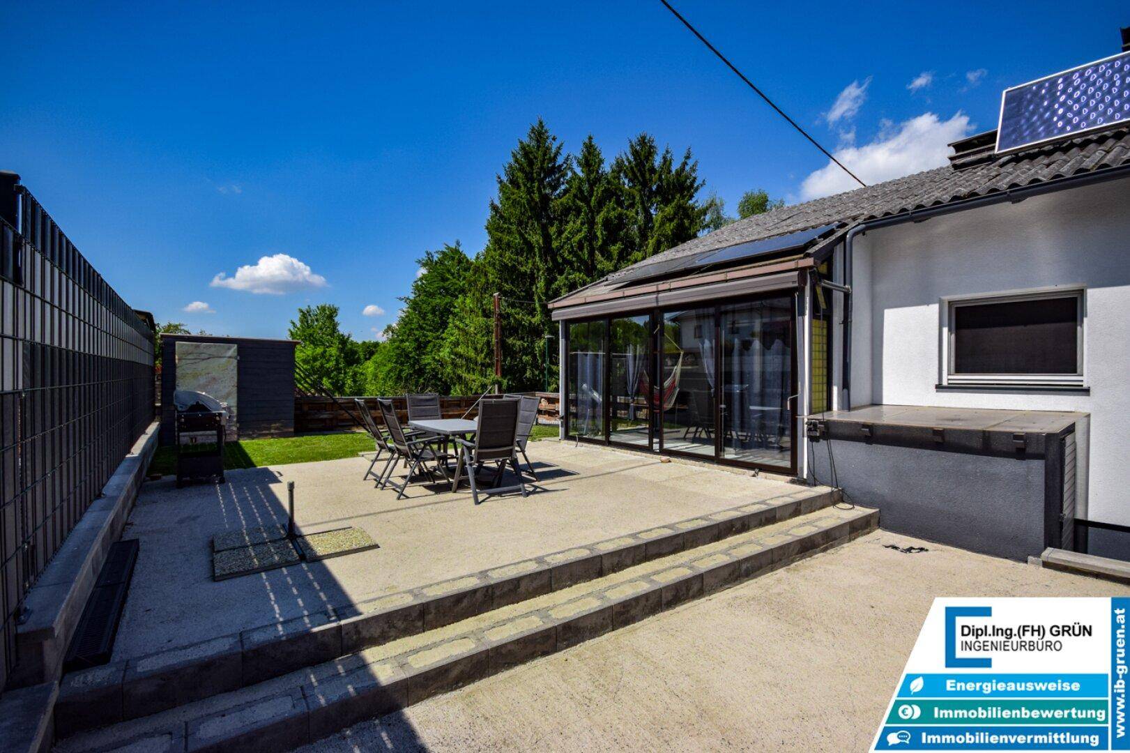 Geräumige Terrasse mit Gartenmöbeln und Grillbereich, angrenzend an einen verglasten Wintergarten.