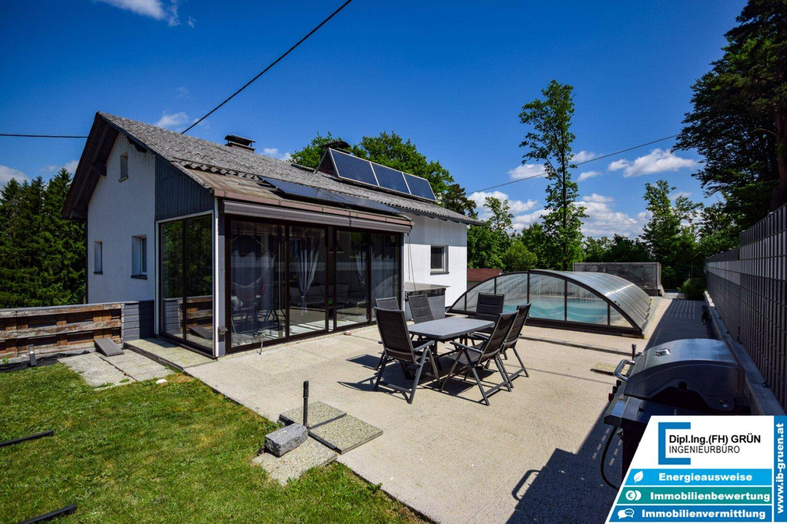 Weitläufige Terrasse mit Sitzgelegenheiten, Grill und Blick auf den überdachten Pool und das Grüne.