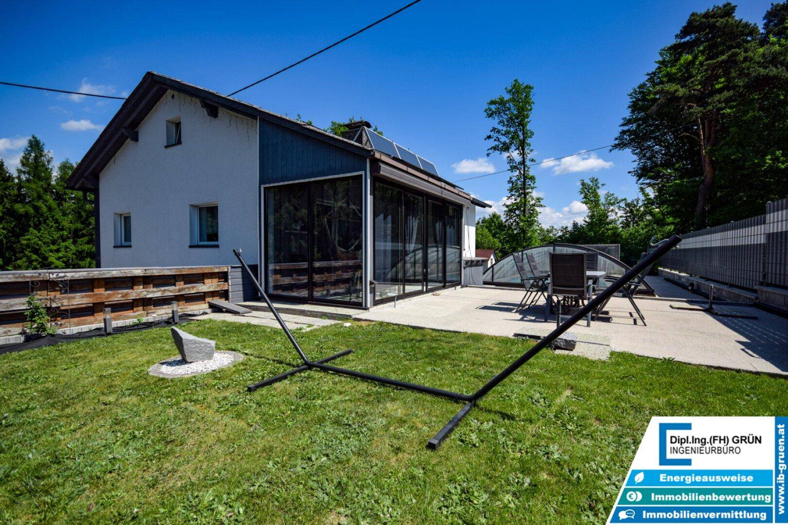 Grüner Gartenbereich mit Hängemattenständer, angrenzend an das Haus mit Wintergarten und Pool.