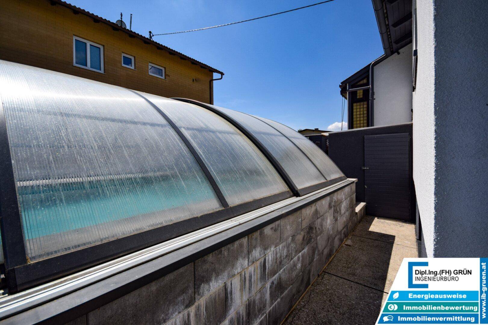 Überdachter Swimmingpool mit transparenter Abdeckung und robuster Umrandung aus Stein.